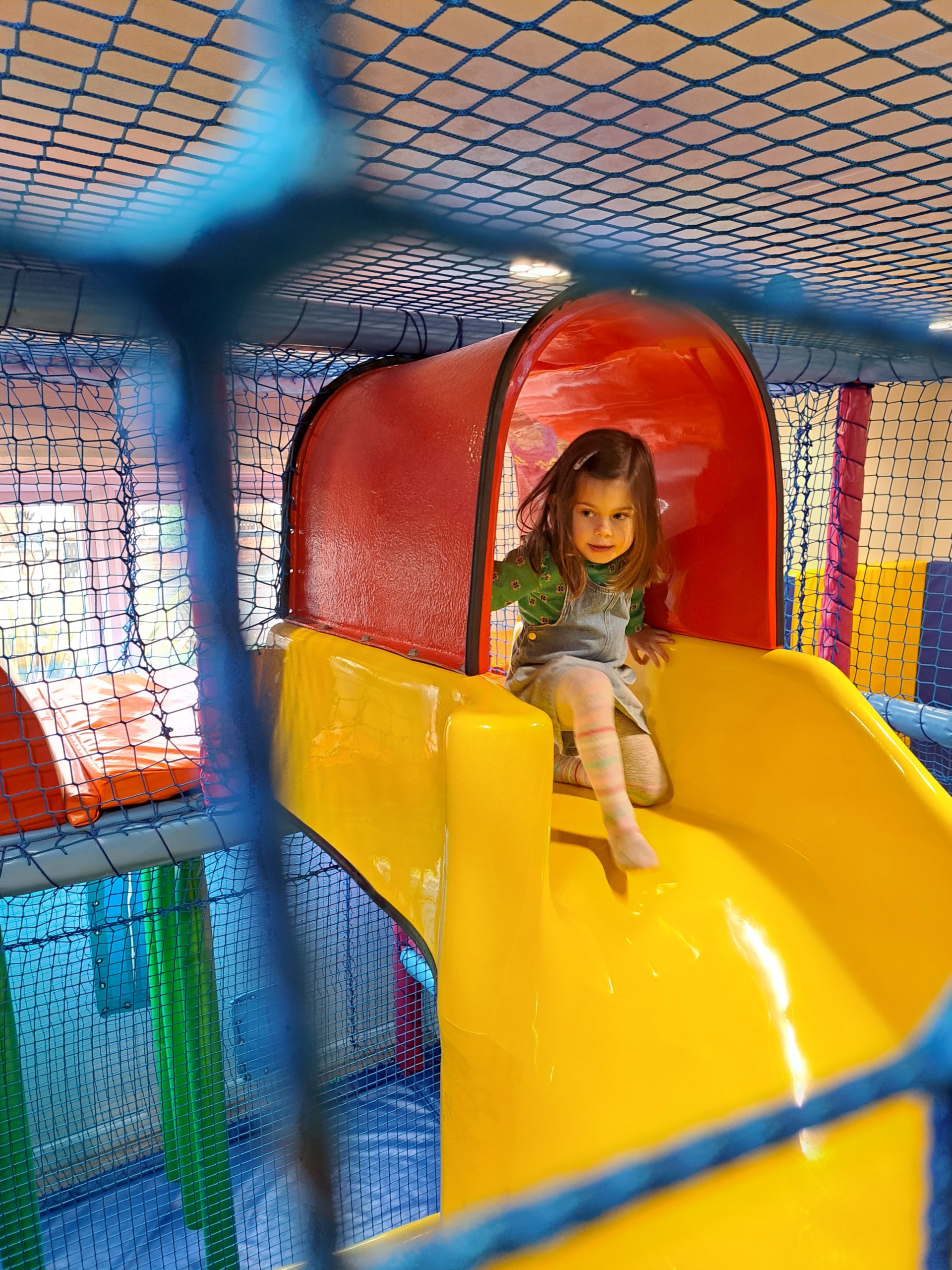 Little girl ready to slide down the big yellow soft play slide.